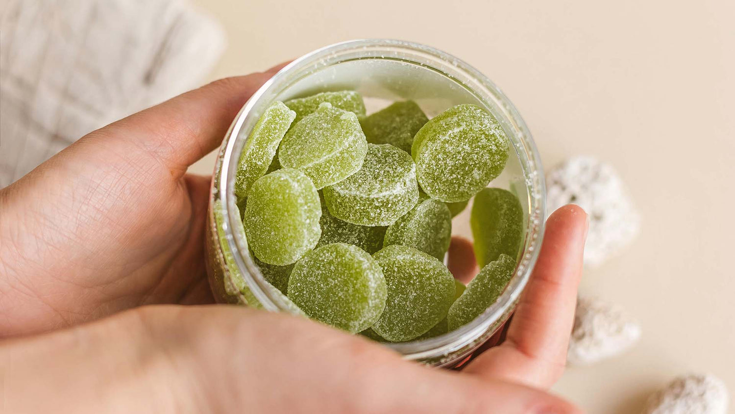 hands of a person holding a jar filled with green-colored gummies