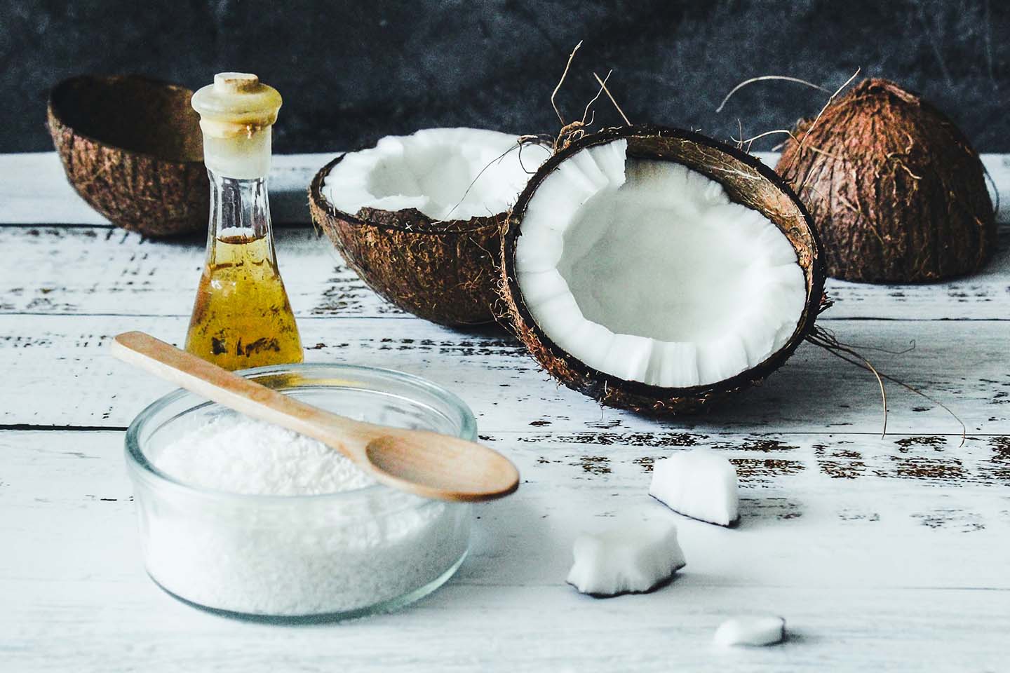 Split open coconut next to bowl of white flakes and jar of oil
