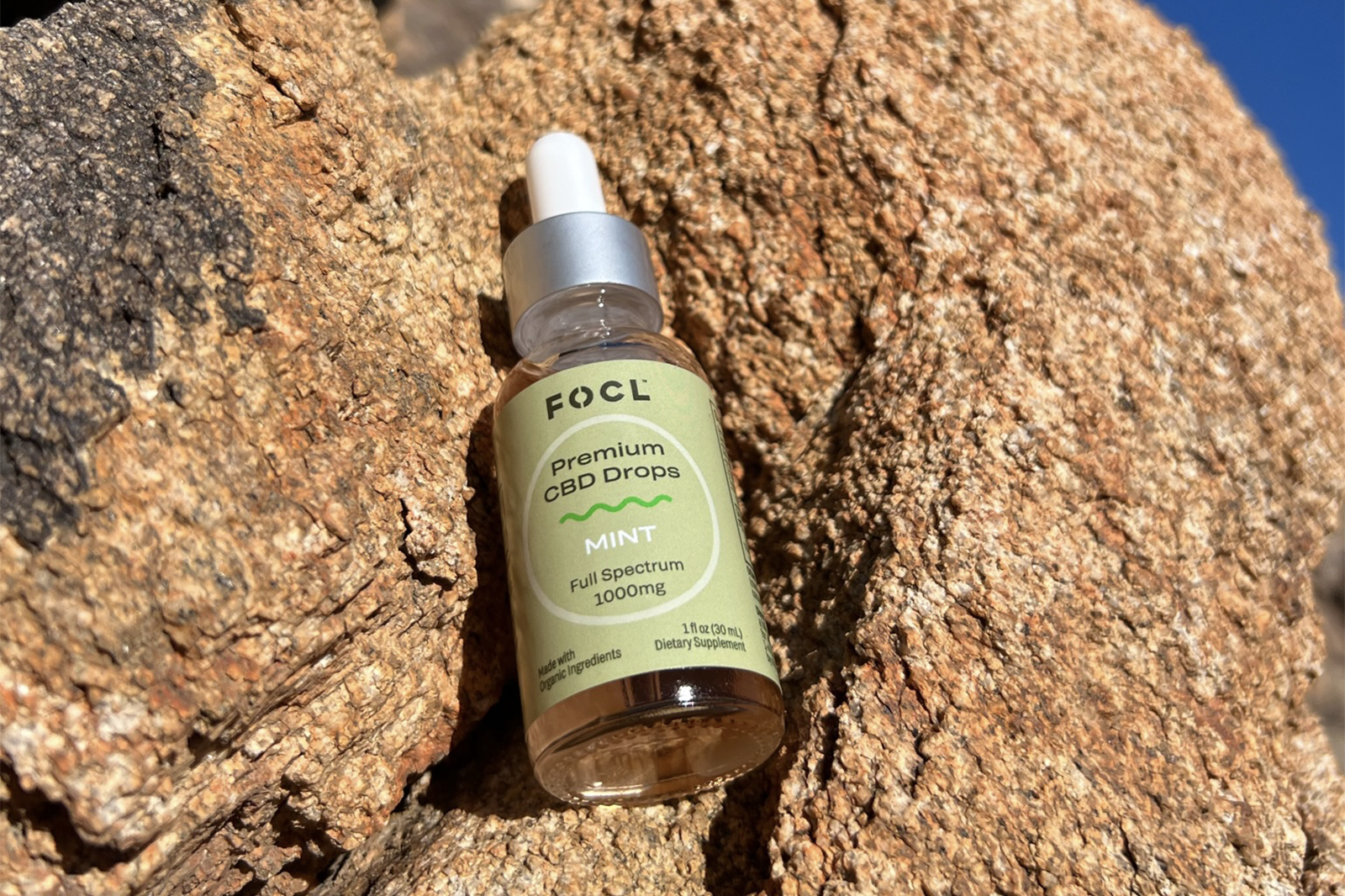 Bottle of FOCL's Premium CBD Drops laying on a rock.