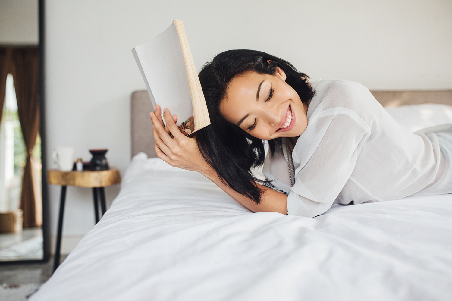 Woman smiling in bed while she reads a book.