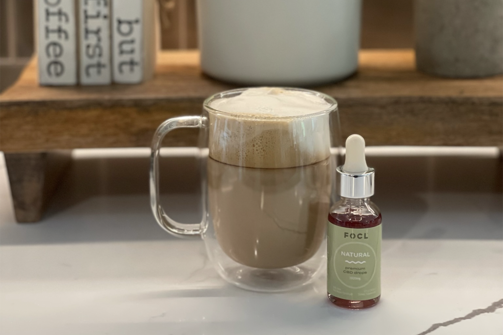 Bottle of FOCL Premium CBD Drops next to a cup of cocoa in front of a bookshelf.