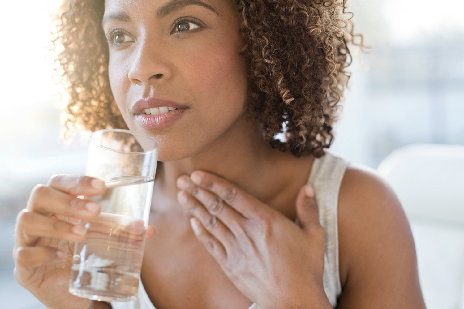 Woman with a hand on her throat and a glass of water on her other hand.