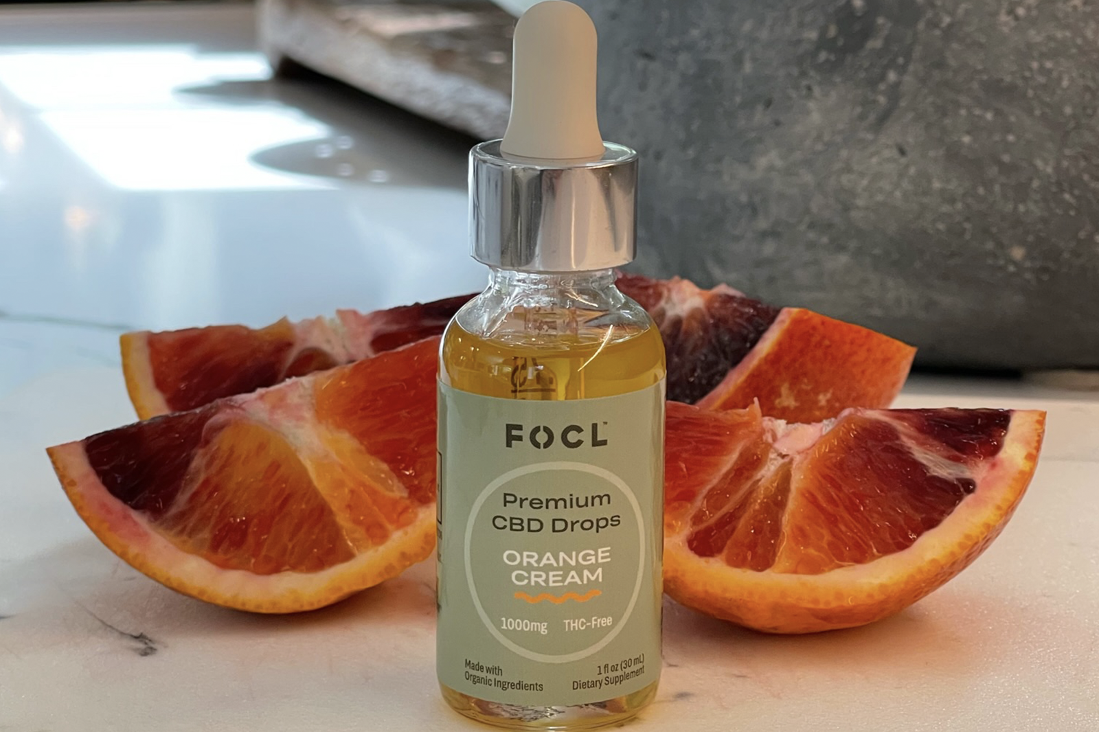 Bottle of FOCL's Orange Cream Premium CBD Drops next to orange slices.