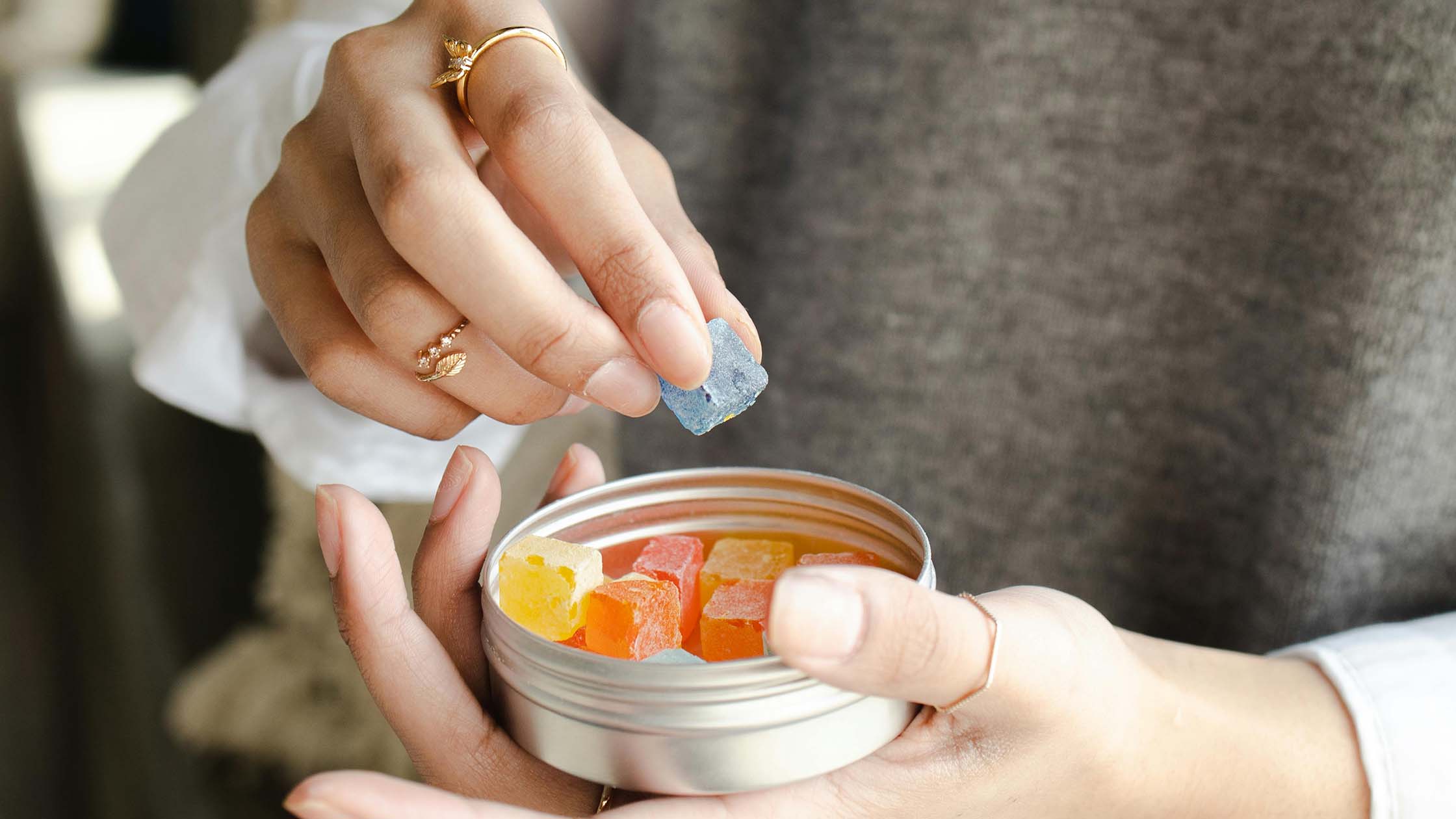 a woman taking a CBD gummy from a metal tin