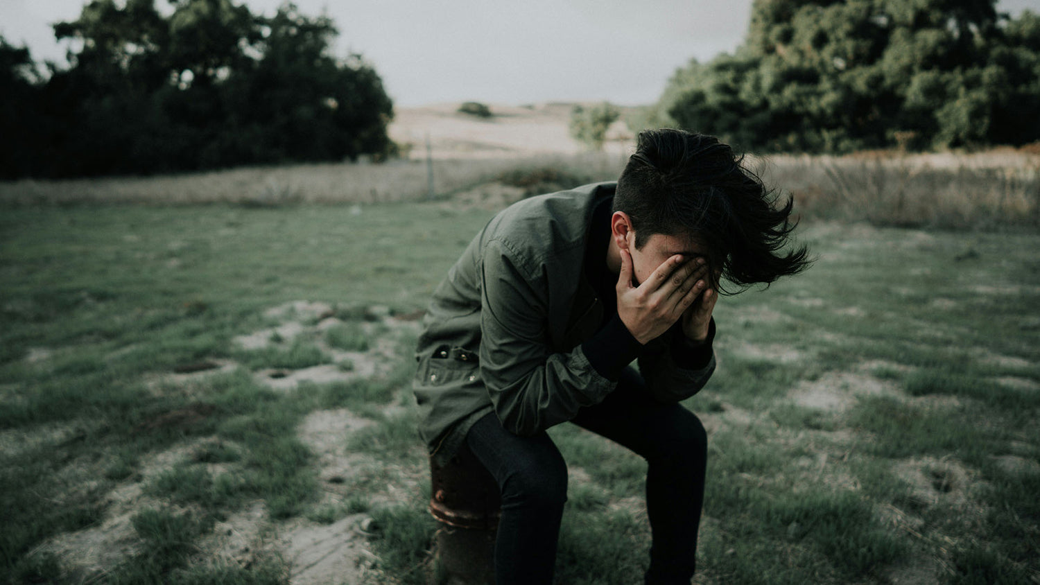 man sitting on a stool outside covering his face with his hands