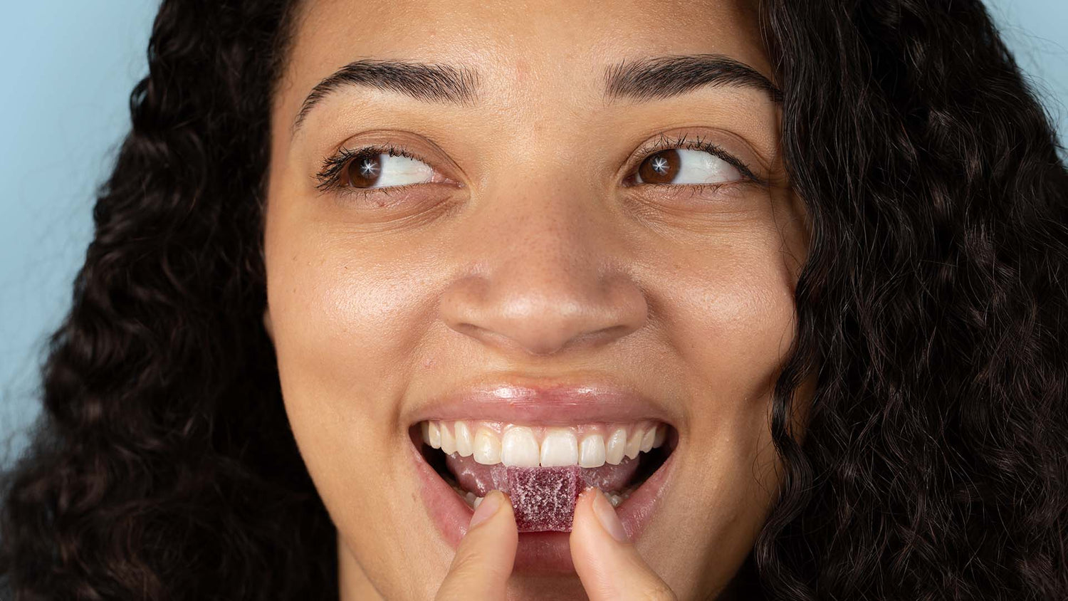 A woman smiling while eating a dark red gummy.