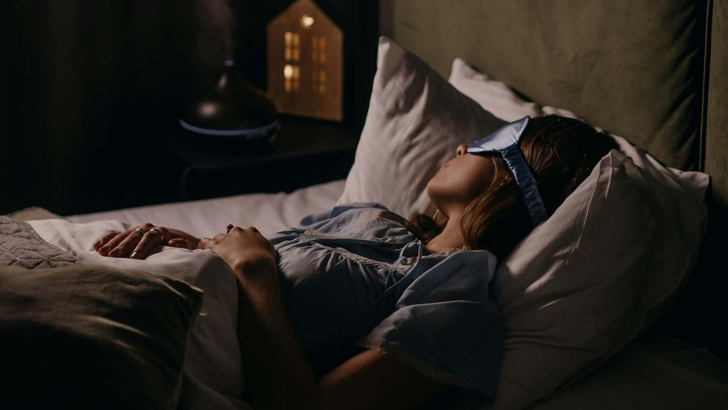 a woman wearing eye mask sleeping on her bed with warm lighting in the background