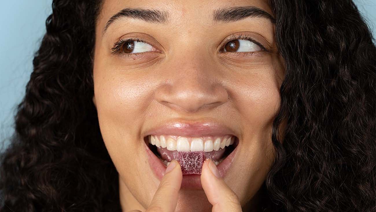 a smiling woman eating a dark red FOCL CBD gummy