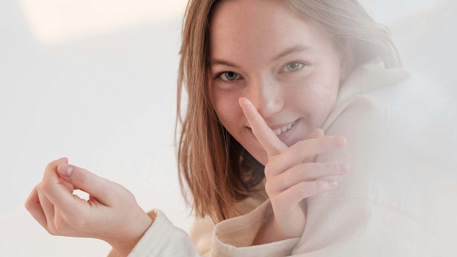 A woman smiles as she gestures with her index finger over her mouth.