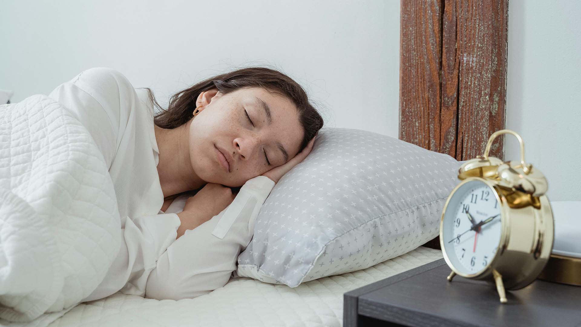 woman sleeping next to an analog alarm clock in the late morning