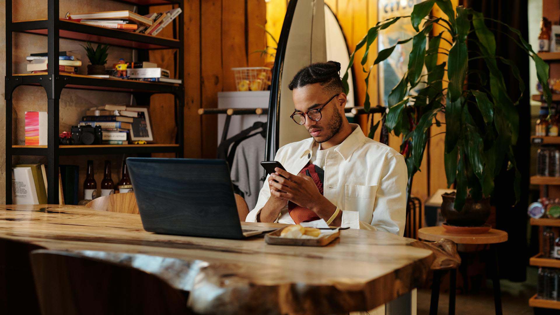 man using his phone at a table with a laptop