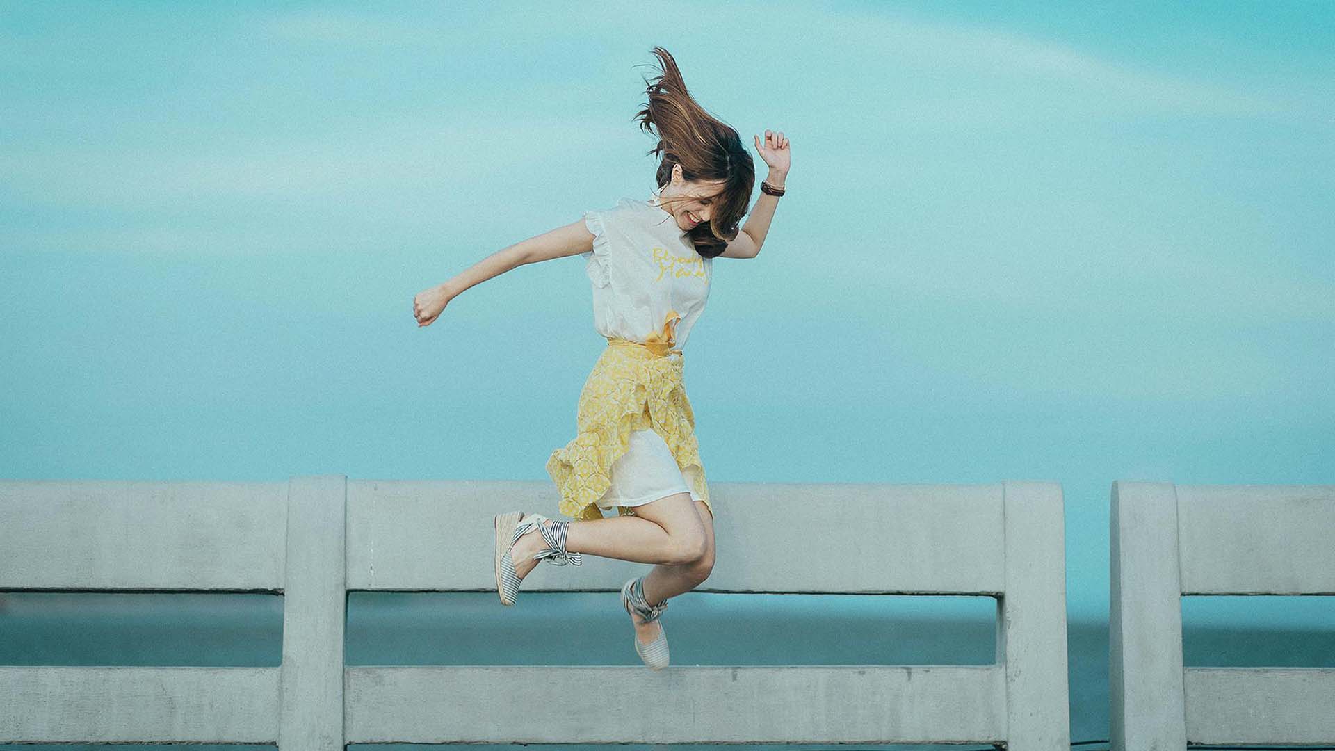 Smiling woman jumping down from a fence