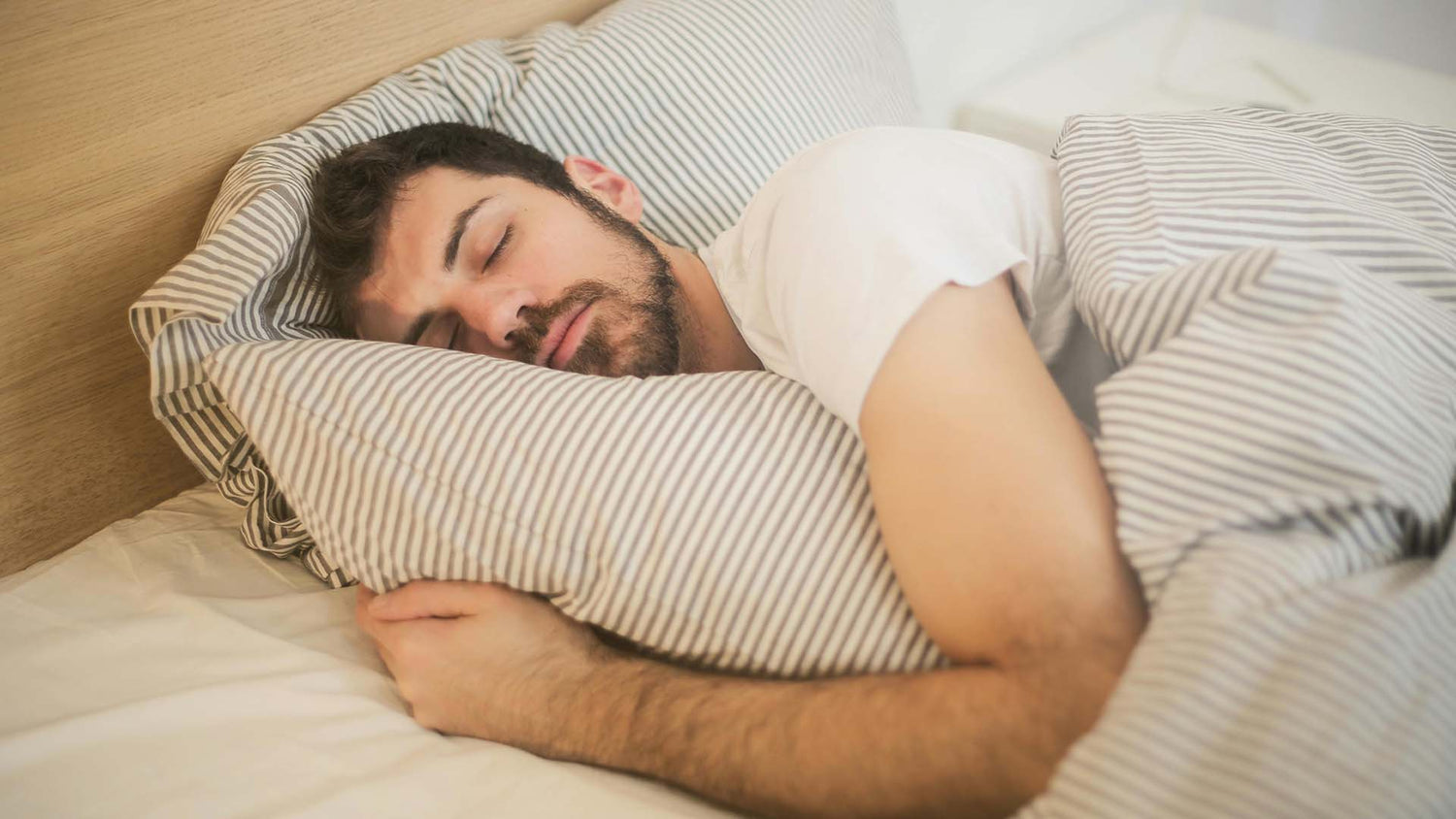 man sleeping peacefully on his side while hugging a pillow