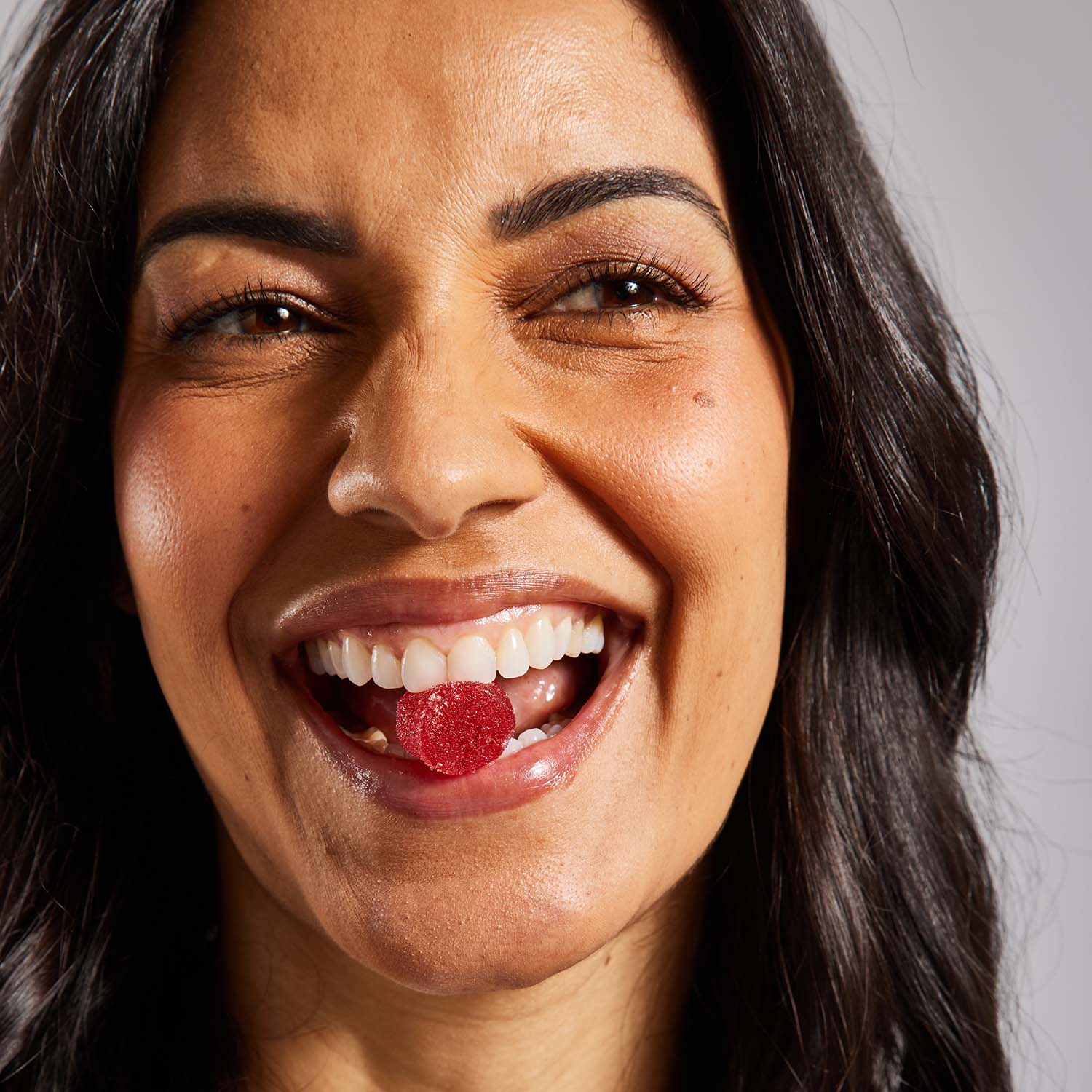 smiling woman biting into a red CBD gummy