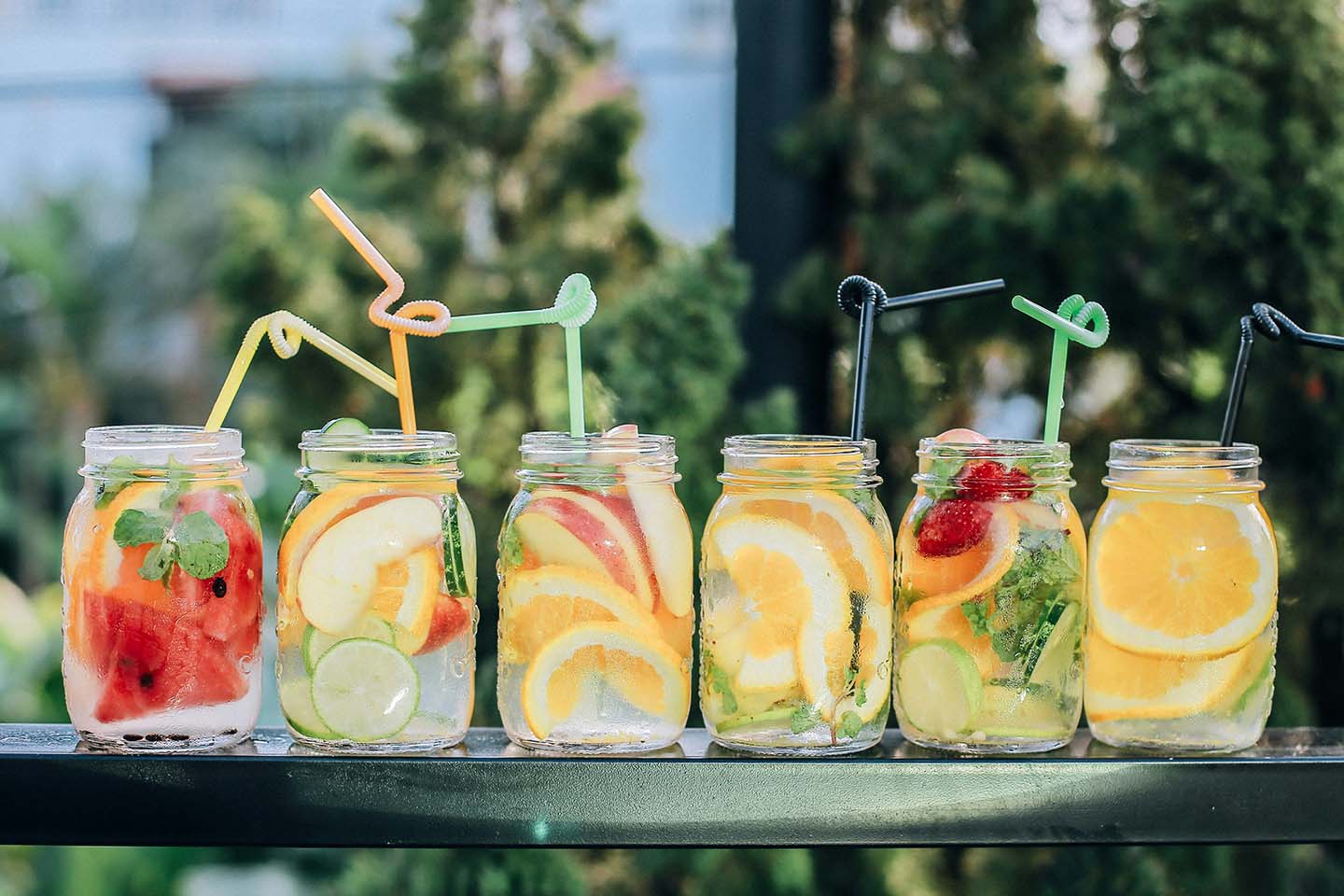 six clear glass mason jars filled with juice with fruit slices