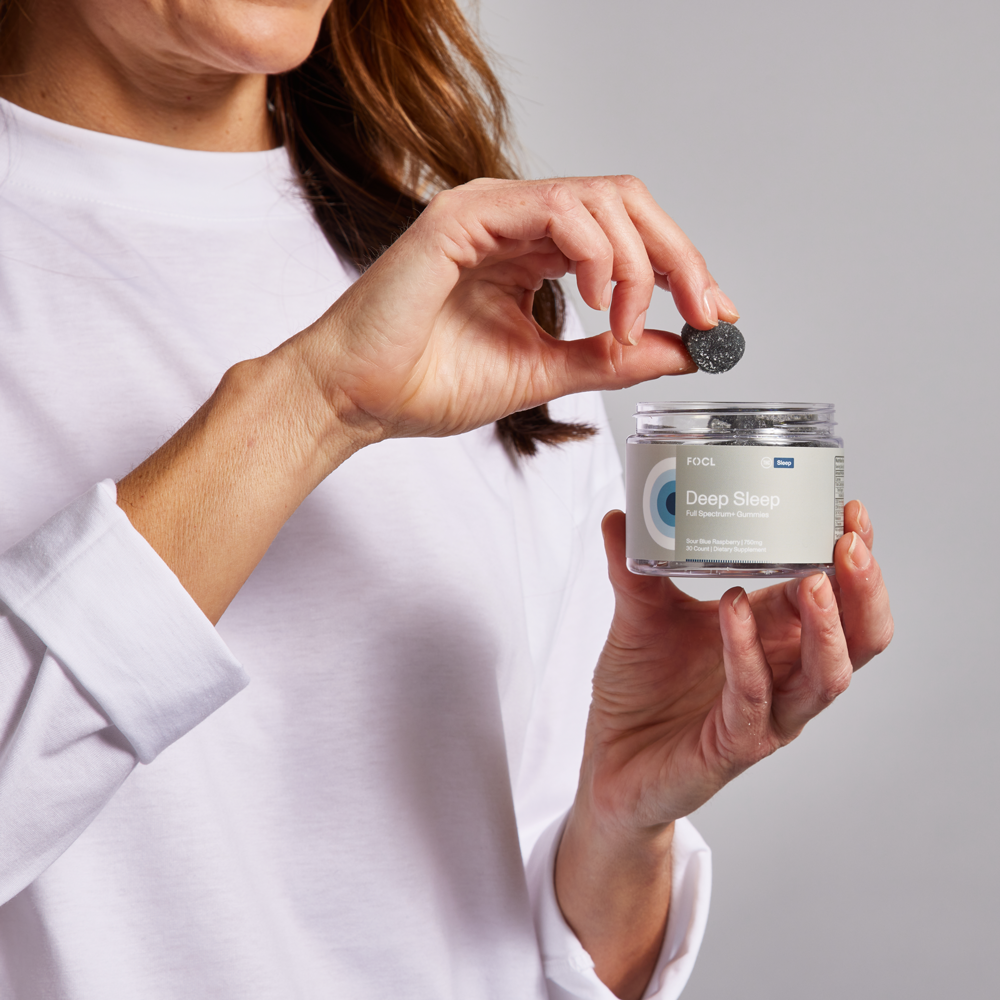 Person holding a jar of FOCL Deep Sleep gummies, taking one out.