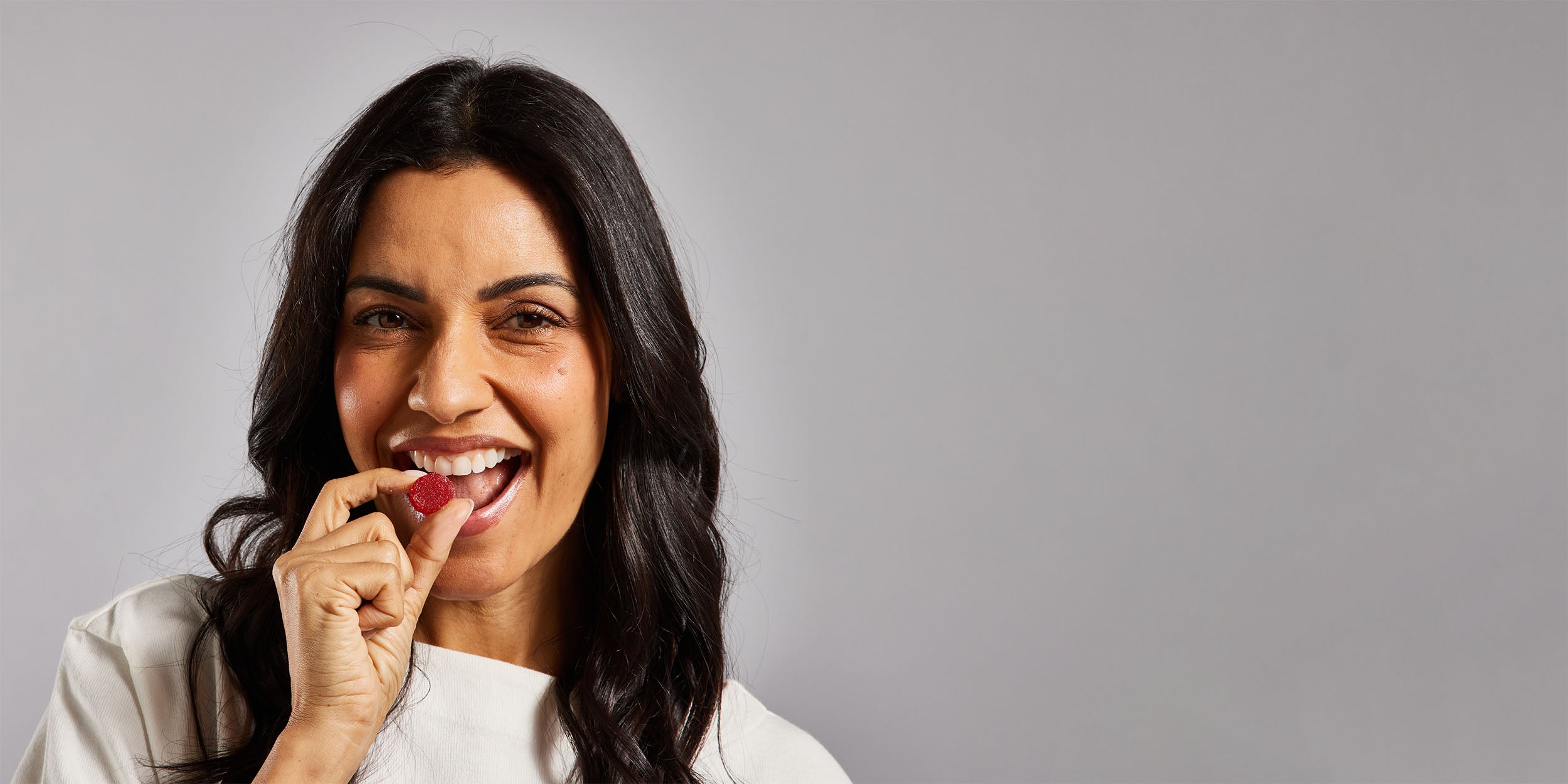 A smiling woman about to eat a red gummy