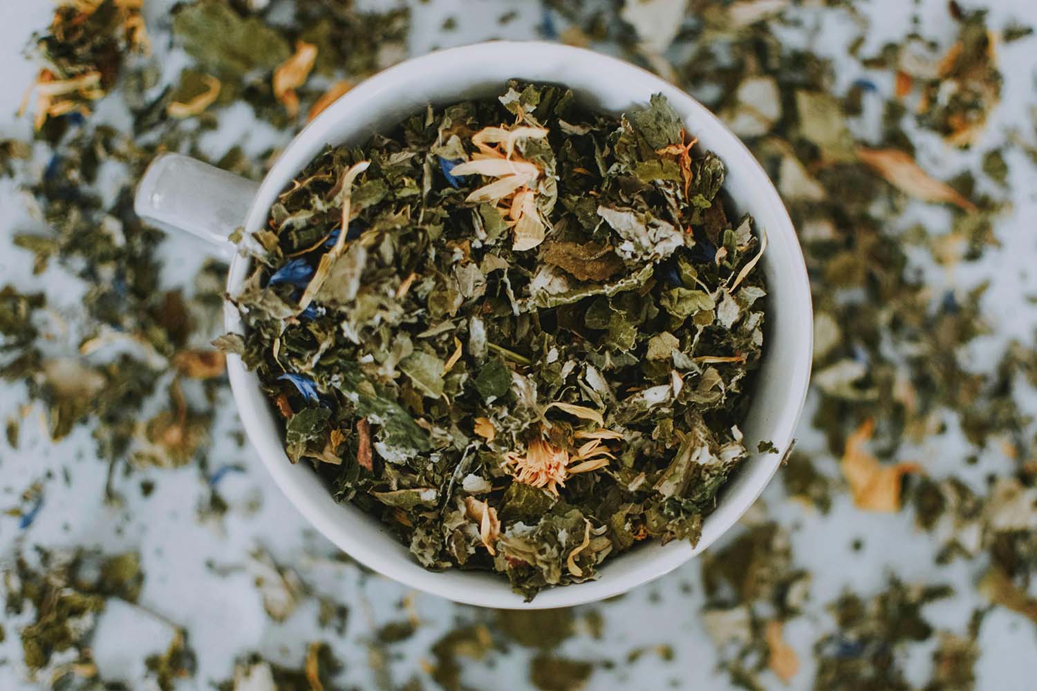 Tea cup overflowing with dried green tea leaves