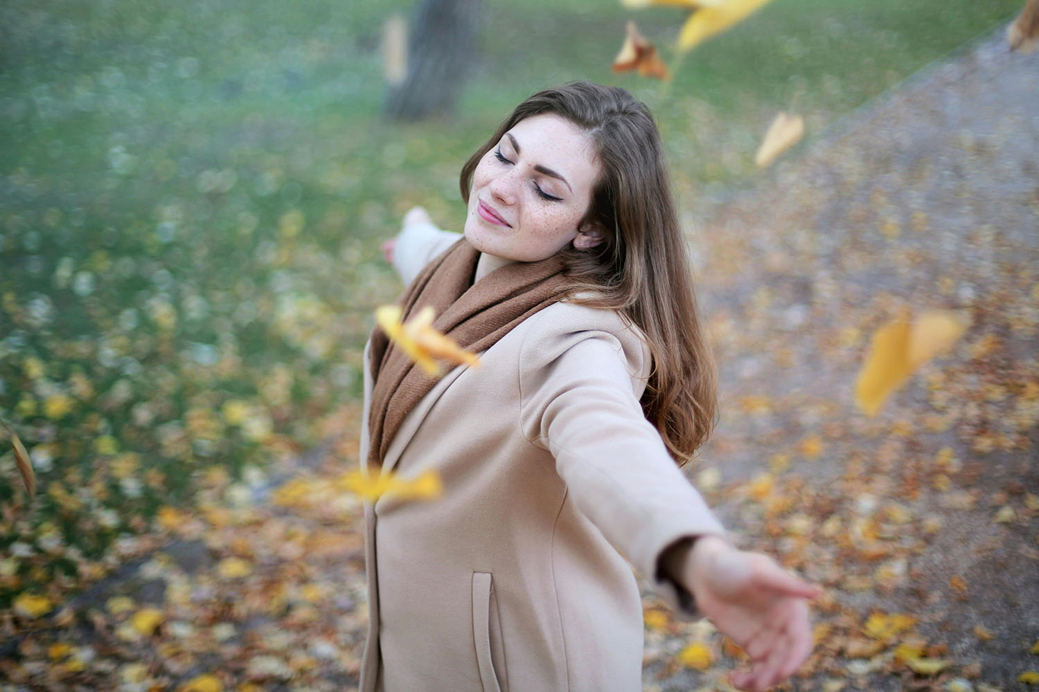 Woman holding her arms outstretched among falling leaves