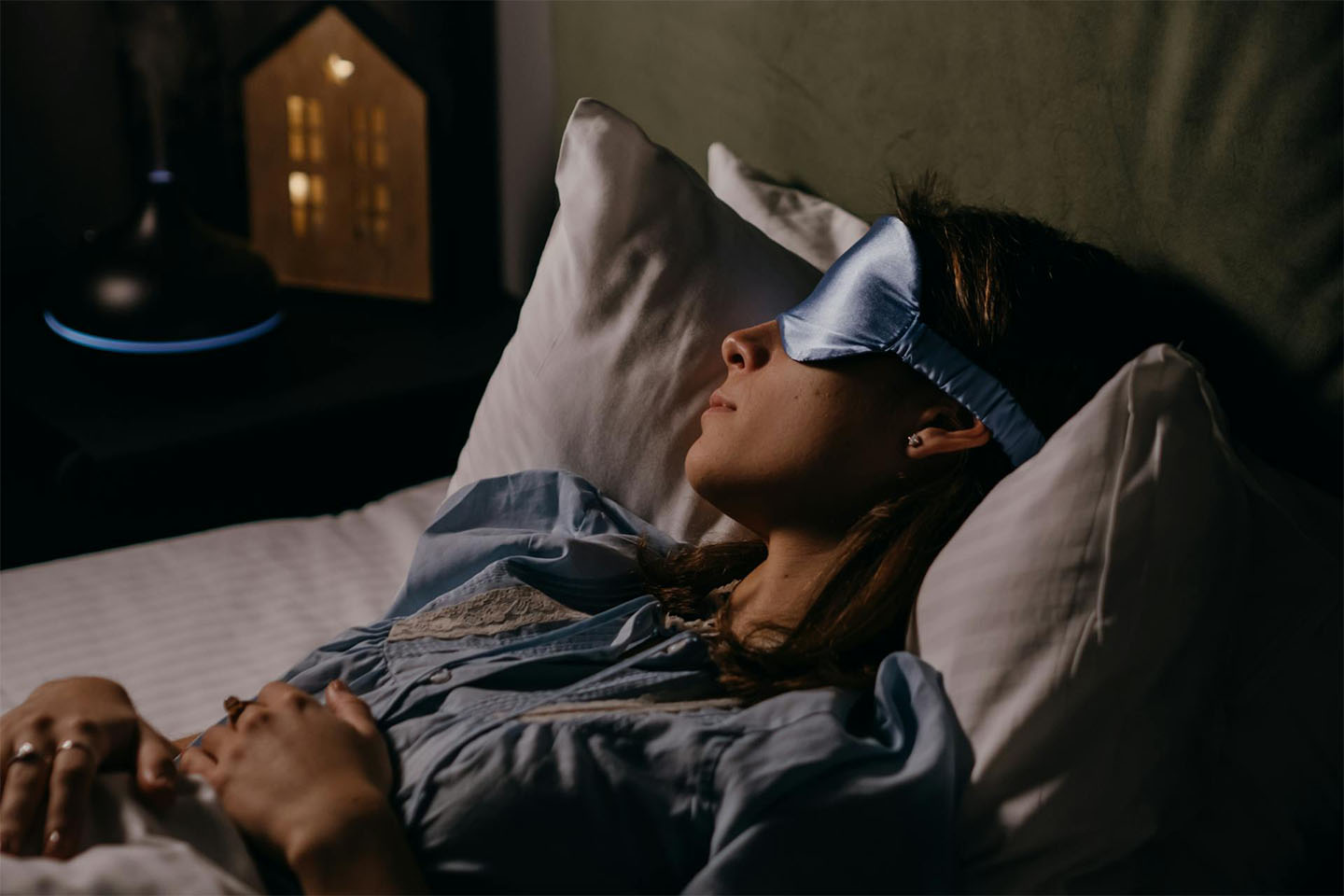 woman wearing eye mask while deeply sleeping in bed with dim lights