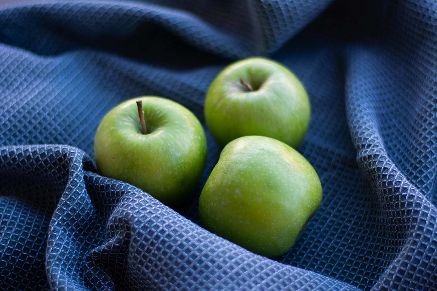 three green apples placed on a blue fabric