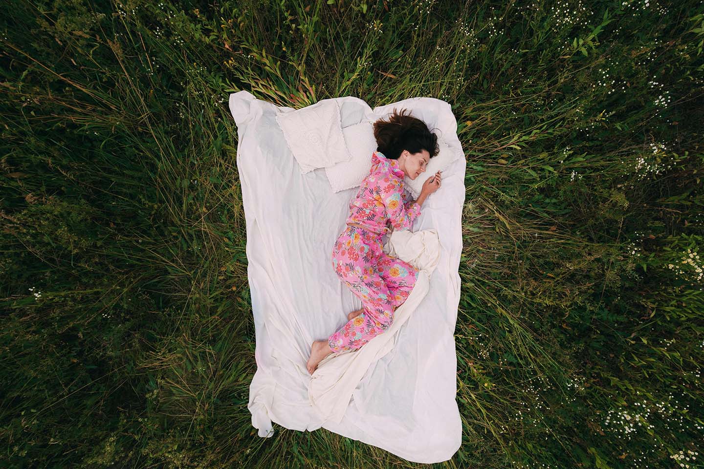 woman deeply sleeping on white blanket in the middle of a grass field