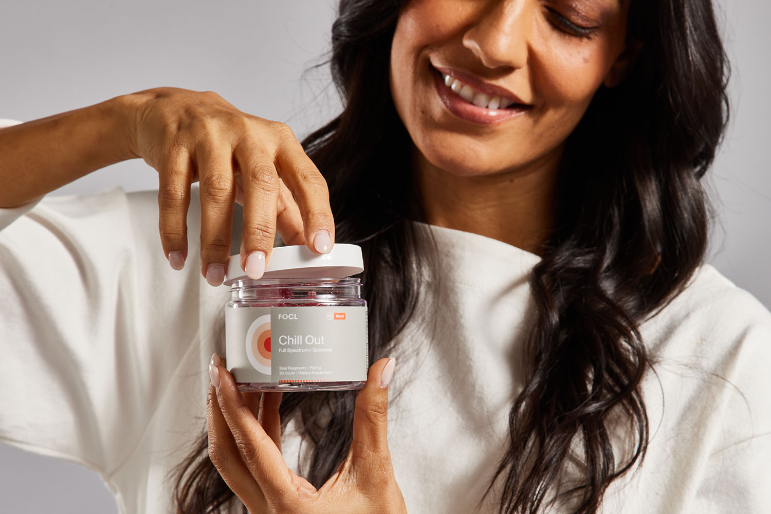 A woman happily opening a jar of FOCL Chill Out Gummies