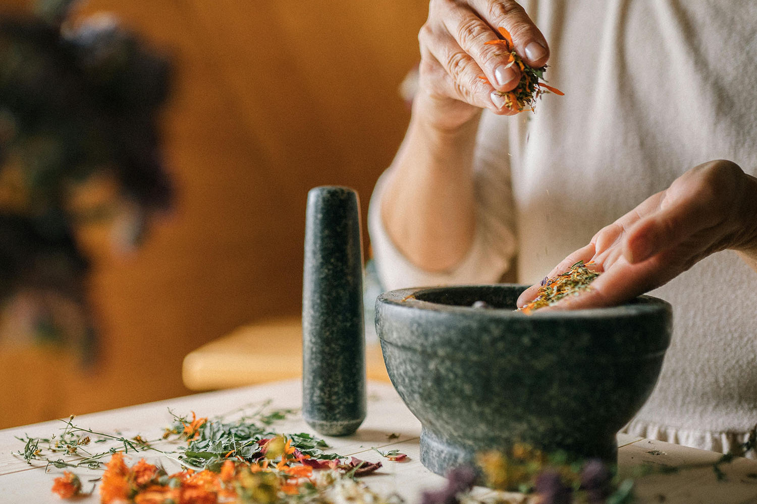 Person adding dried flowers and herbs to a mortar and pestle