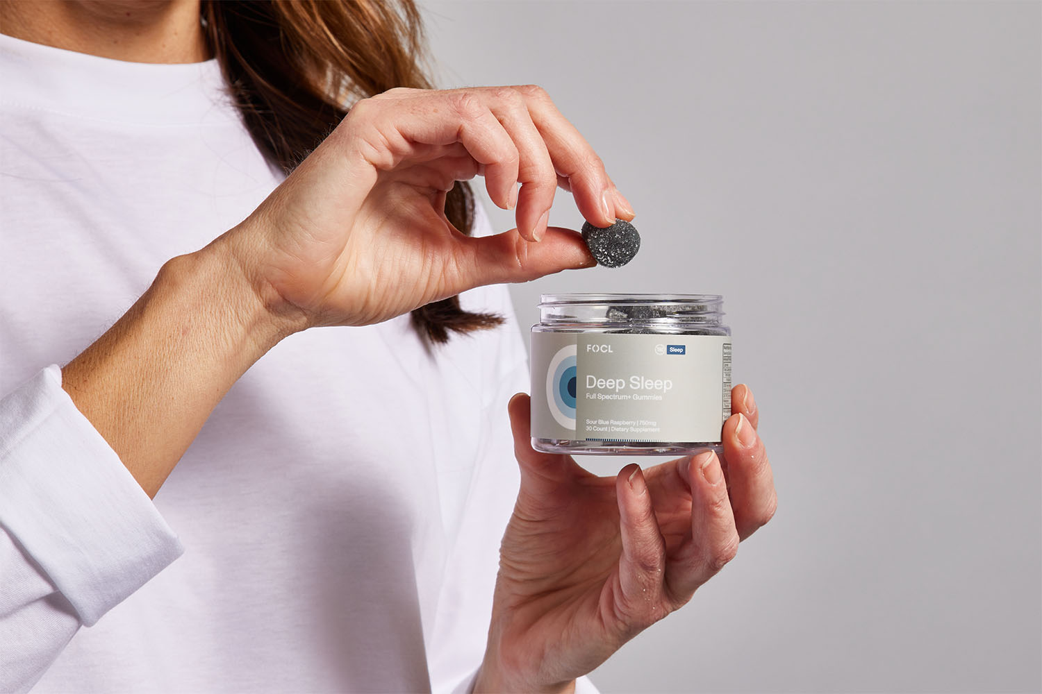 Woman holding jar of FOCL Deep Sleep gummies