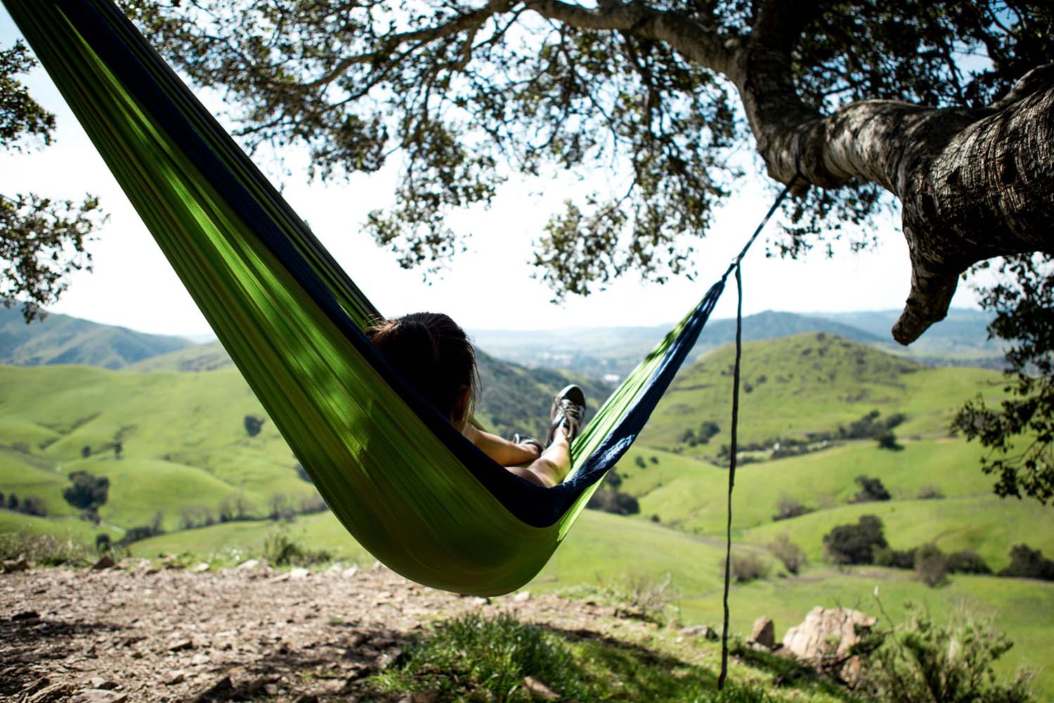 Person lying in green hammock overlooking grassy hills