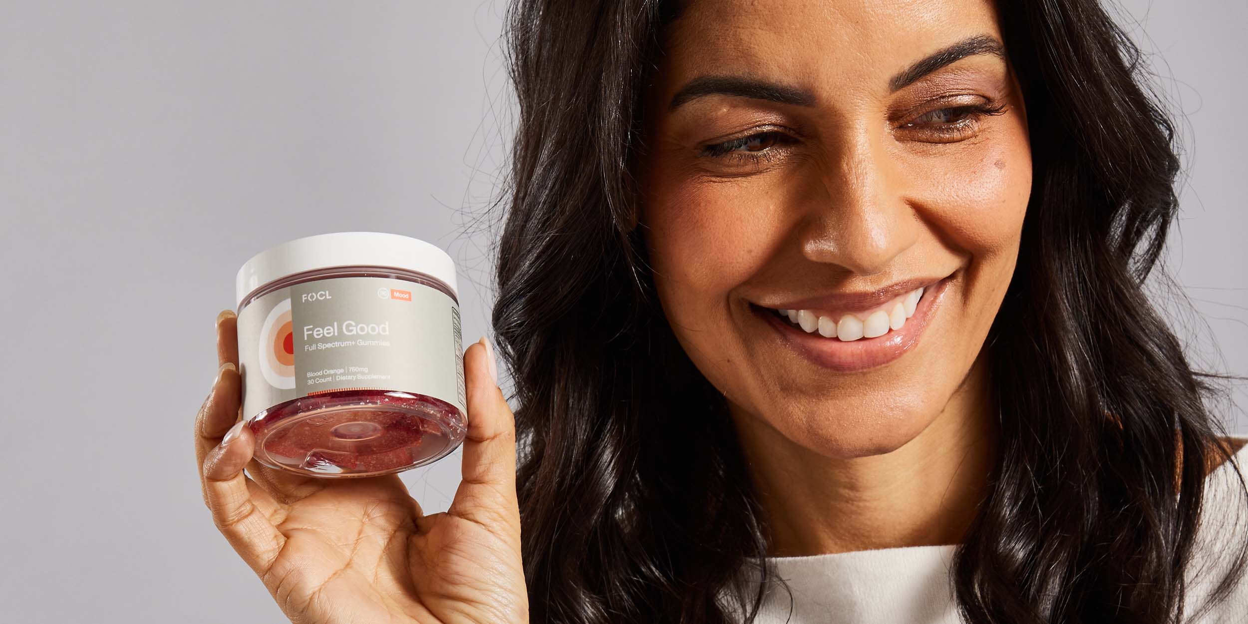 A smiling woman holding a jar of FOCL Feel Good gummies