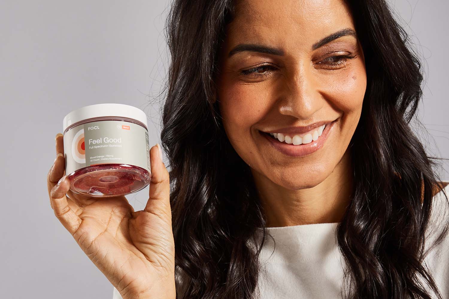 A smiling woman holding a jar of FOCL Feel Good gummies