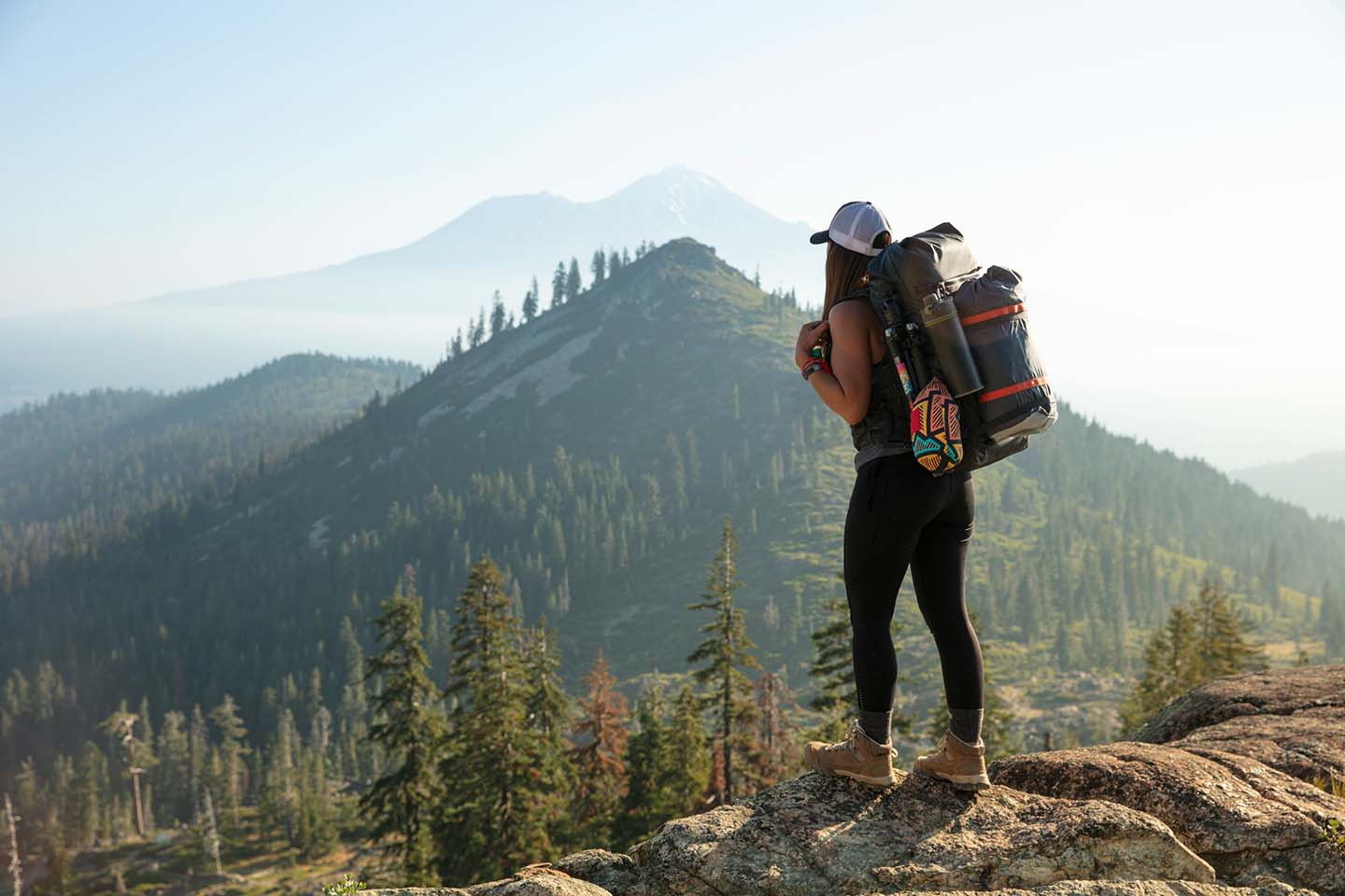 Hiker with a backpack standing on a rocky surface overlooking a mountain range