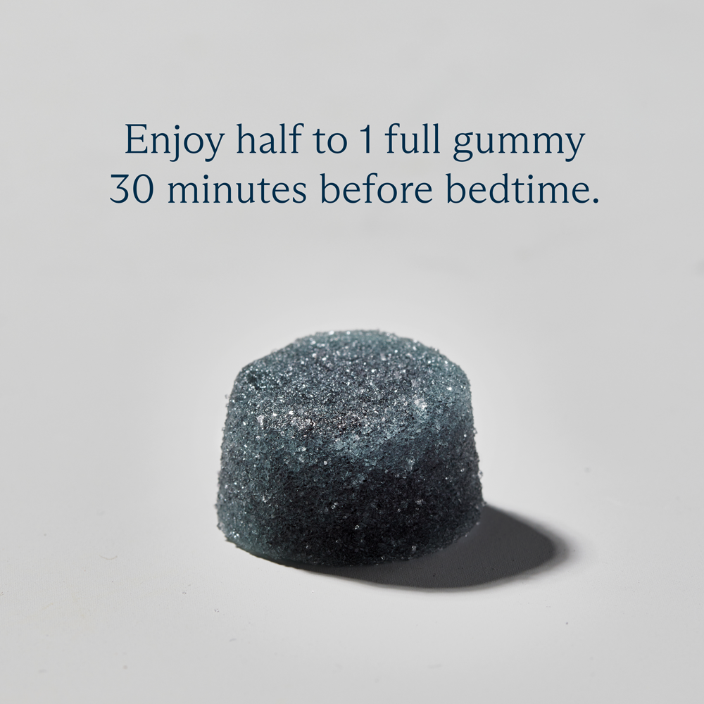 Blue gummy on white surface with text, 'Enjoy half to 1 full gummy 30 minutes before bedtime.'