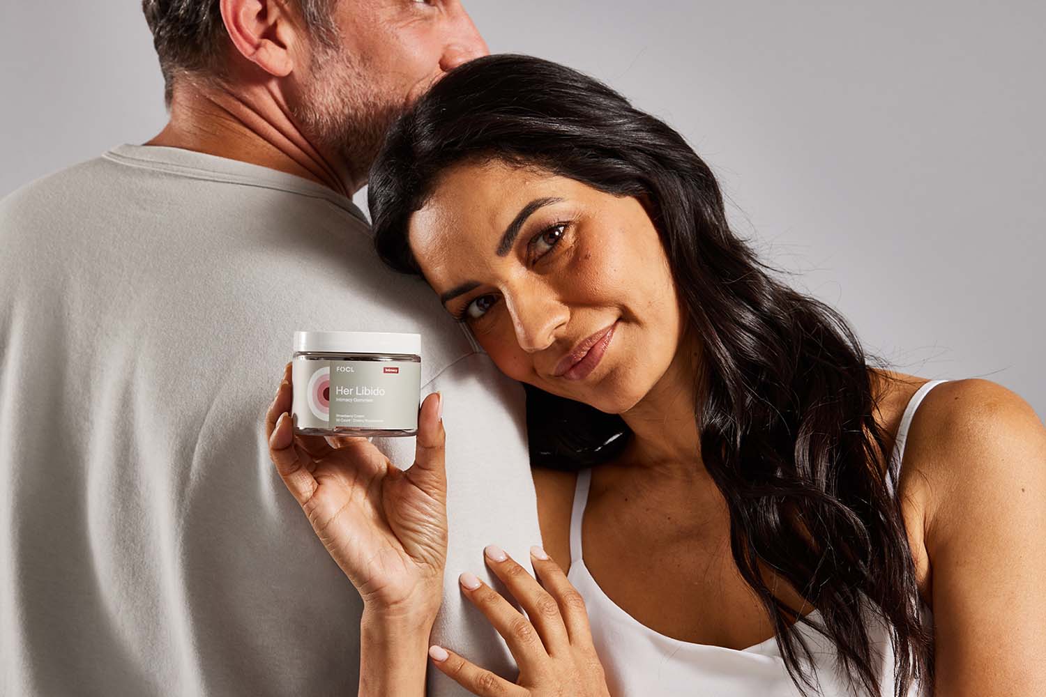 Woman holding jar of FOCL Her Libido gummies while leaning on a man's shoulder